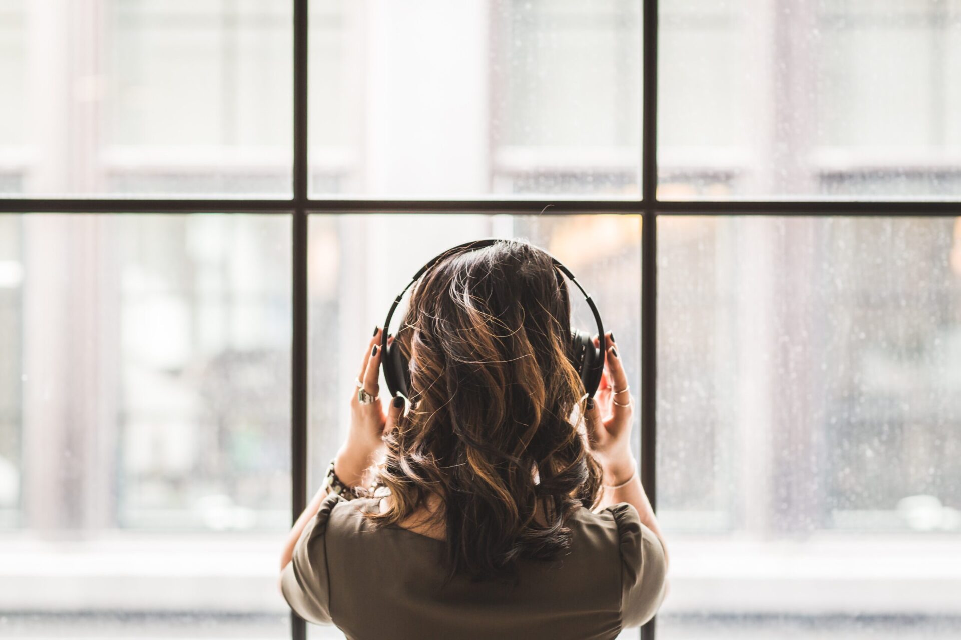 Une femme écoute de la musique dans un casque audio en regardant la fenêtre.