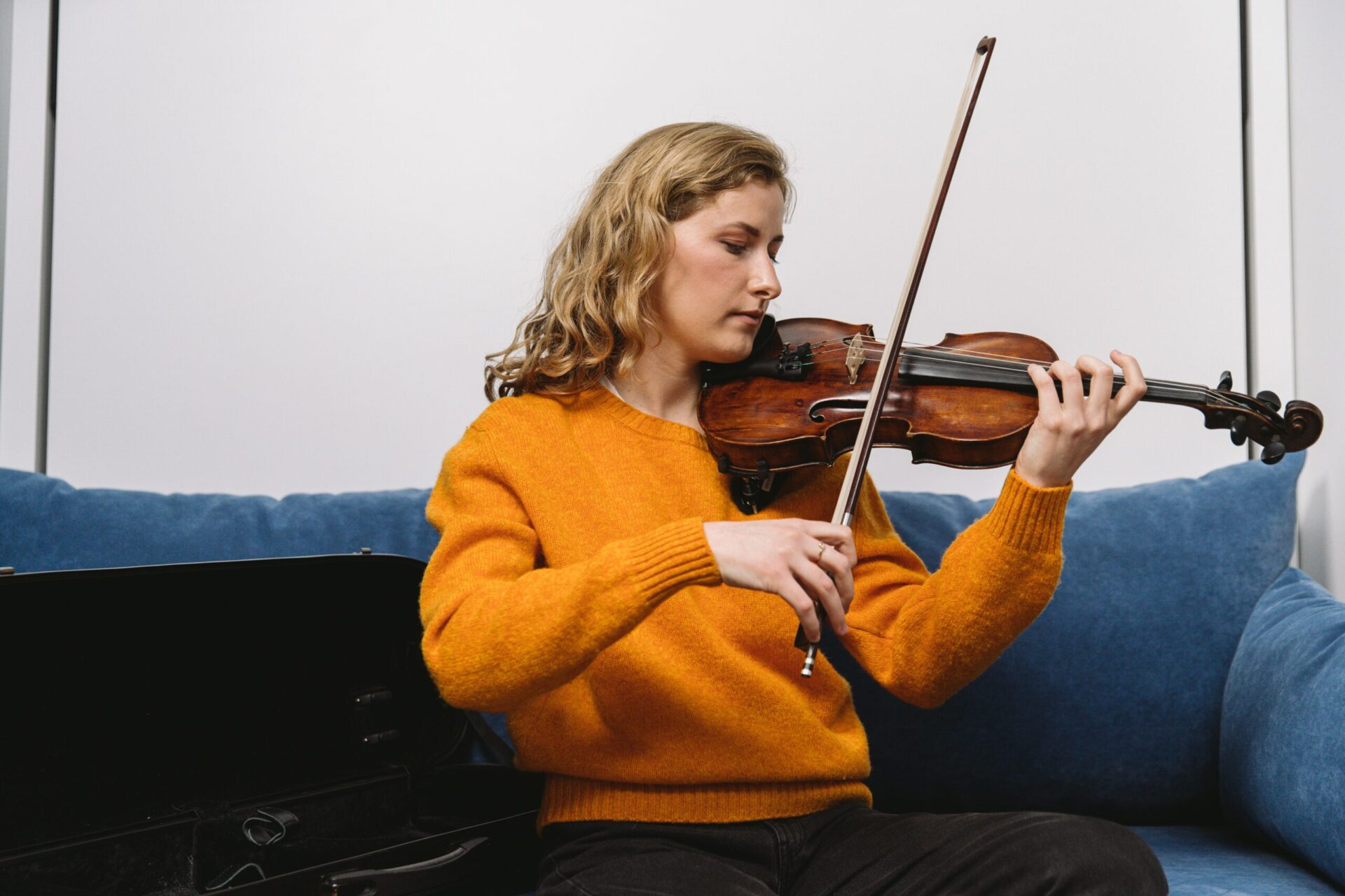 Une jeune femme joue du violon assise sur un canapé
